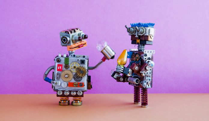 Robots communication, artificial intelligence concept. Two robotic characters with light bulbs. Creative design toys on pink wall, brown floor background.
