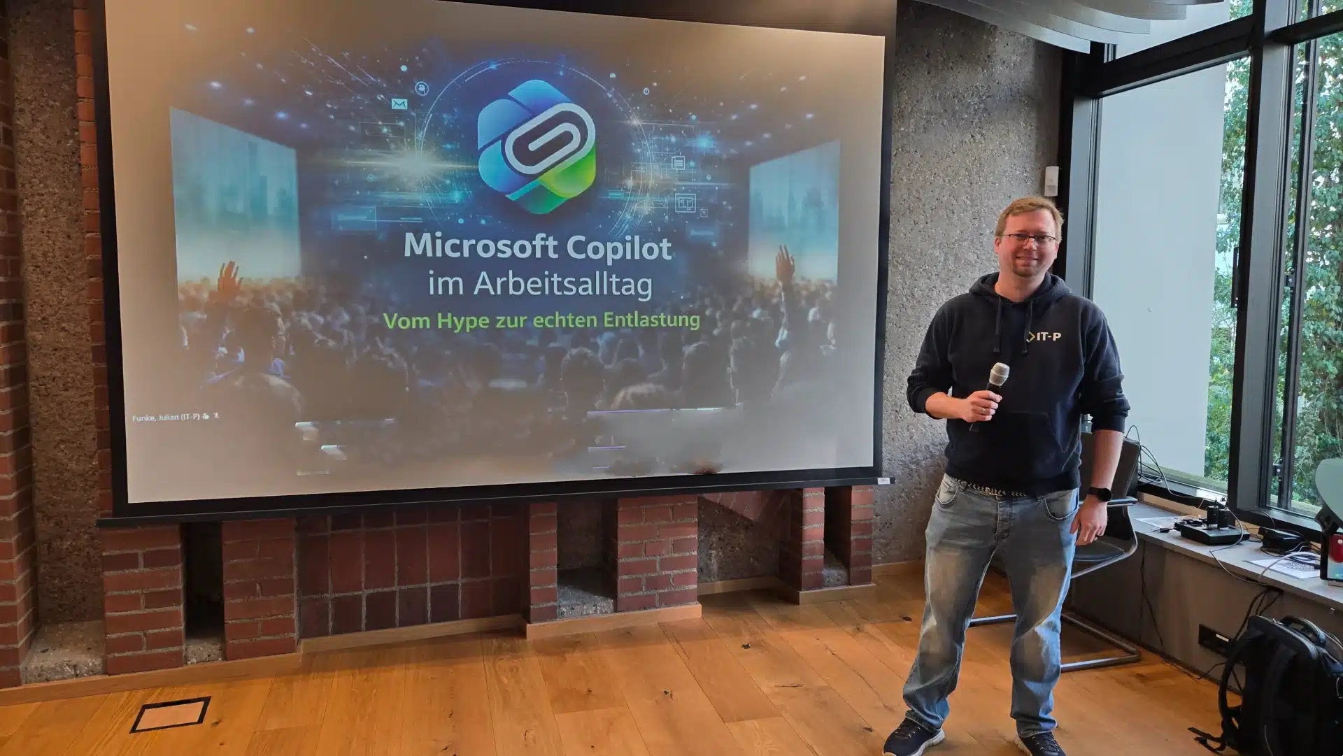 Gundlach Keynote Julian Funke - KI-Speaker und Experte für Künstliche Intelligenz Mann mit Mikrofon steht neben großer Bildschirmprojektion mit Vortrag über Microsoft Copilot im Arbeitsalltag (Vom Hype zur echten Entlastung).